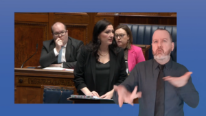 Deputy First Minister, Emma Little-Pengelly, answers questions put to the Executive Office during Plenary. In this still image of Ms Little-Pengelly providing an answer, an ISL interpreter is pictured during his translation of the footage.