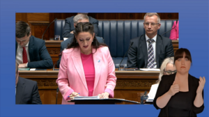 Still shot from the Assembly Chamber showing the deputy First Minister, Emma Little-Pengelly answering a question during Question Time. In the foreground, an Irish Sign Language interpreter is shown providing interpretation.
