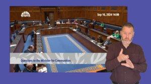 Communities Minister Gordon Lyons answering questions on during Question Time. An ISL interpreter is signing in the foreground.