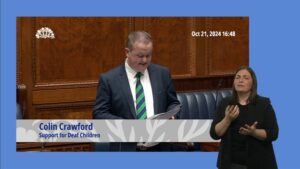 Colin Crawford MLA speaking in the Assembly Chamber. In the foreground is a BSL interpreter.