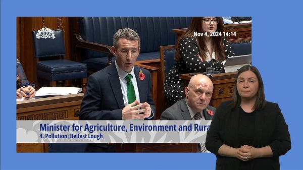 Minister Andrew Muir answering questions in the Assembly Chamber. In the foreground, a BSL interpreter interprets Mr Muir's answers.