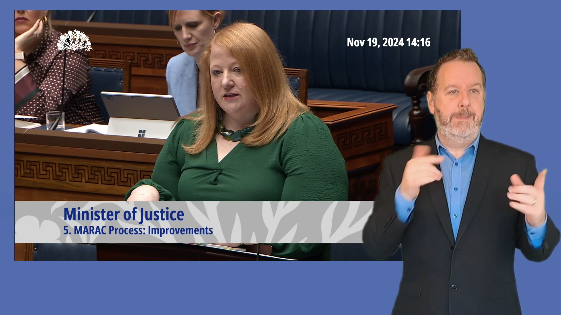 A screenshot of Minister for Justice, Naomi Long, answering questions during Question Time in the Assembly Chamber on Tuesday 19 November 2024. In the foreground an ISL interpreter is providing interpretation.