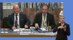 Representatives of teh Department for Communities providing evidence to the Committee for Communities on the progress of the Sign Language Bill. In the foregraound we see a BSL interpreter.