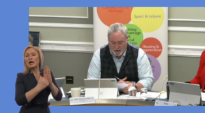 Chairperson Colm Gildernew during the meeting of the Committee for Communities on Thursday 6 February 2025. In the foreground we see an ISL signer providing interpretation.