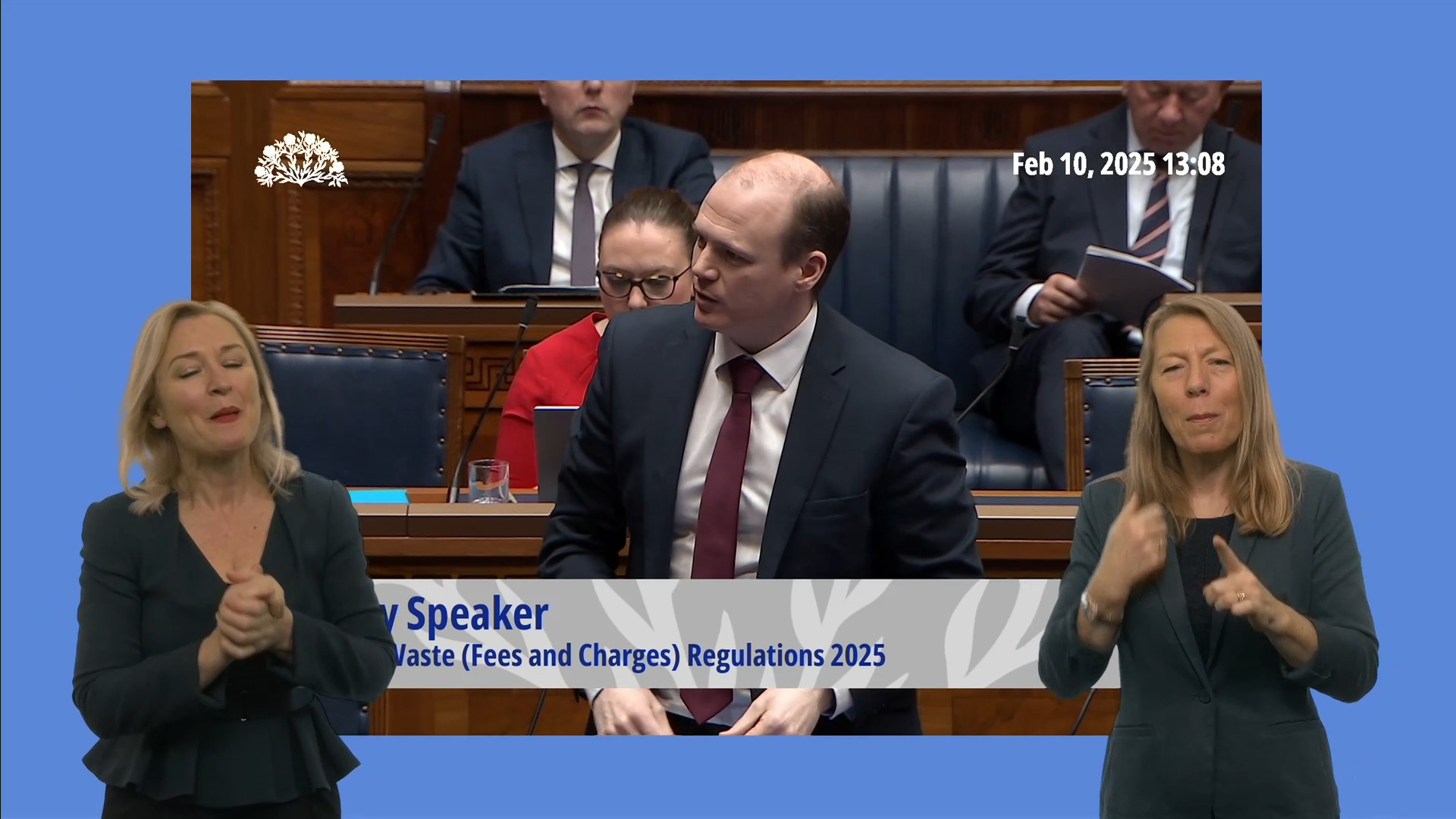 Minister for Communities, Gordon Lyons, introducing the Sign Language Bill. In the foreground we see an ISL interpreter on the left and a BSL interpreter on the right.